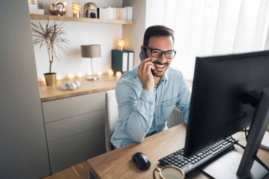 A remote worker sat at a home desk, speaking on the phone. 